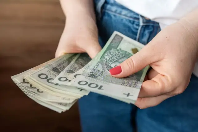Dłonie trzymające stos banknotów 100 zł. Czy to już kwota bazowa służba cywilna 2026?