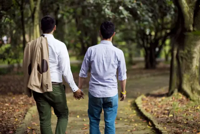 Dwóch mężczyzn idzie ręka w rękę po ścieżce w parku. Ich homoseksualizm jest widoczny w ich bliskości.