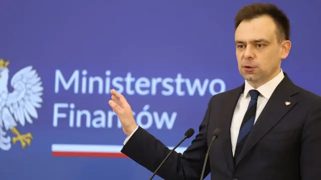 Minister finansów przemawia na tle logo Ministerstwa Finansów.