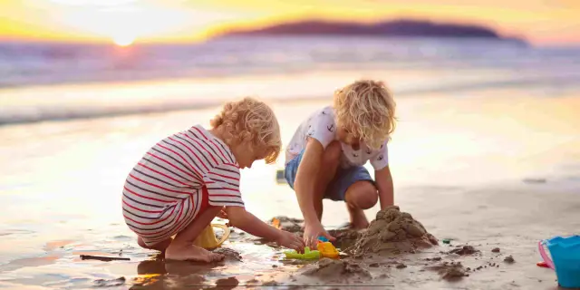 Dwóch chłopców buduje zamek z piasku na plaży podczas zachodu słońca. To nietypowe atrakcje dla dzieci, które zapewniają mnóstwo radości.