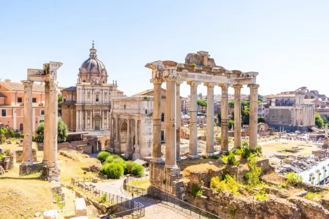 Rzym last minute: ruiny Forum Romanum z kolumnami i łukiem Triumfalnym, w tle kopuła kościoła.