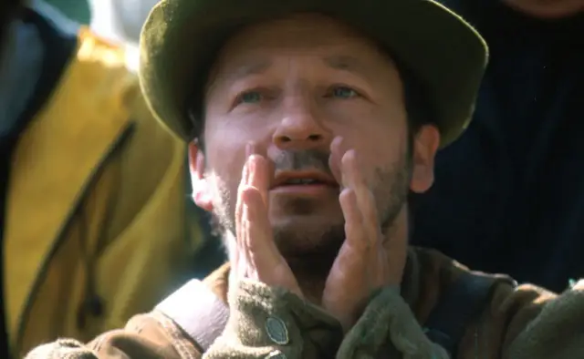 Zbigniew Zamachowski w historycznych filmach, z dłońmi przy twarzy, w zielonym kapeluszu.