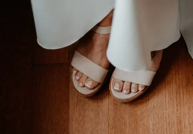 Stopy w sandałach, z idealnym pedicure french. Delikatne paski sandałów i biel sukni tworzą subtelny kontrast.