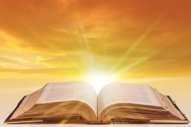 Otwarta Biblia, z której wydobywa się światło, niczym niesamowite cytaty z biblii rozświetlające niebo.