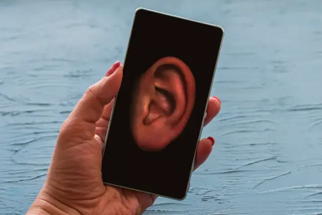 Dłoń trzyma smartfon z uchem na ekranie. Czy Twój telefon jest na podsłuchu?
