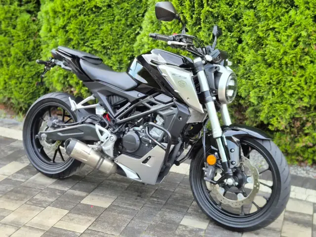 Czarny motocykl Honda z serii CBR, z chromowanym wydechem LeoVince, stoi na kostce brukowej przed żywopłotem.