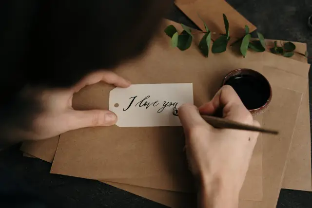 Piszę list do dziewczyny. Na białej etykiecie piórem z kałamarza tworzę napis "I love you".