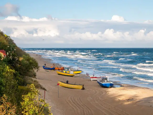 Piękna plaża w Rewie i okolicy, z kolorowymi łodziami na piasku i falującym morzem. Idealne miejsce na spacer i podziwianie widoków.