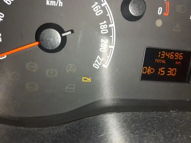 Kontrolki w Oplu: ABS, hamulec ręczny, ciśnienie oleju, poduszka powietrzna, drzwi, bagażnik. Na wyświetlaczu 134696 km i czas 15:30.