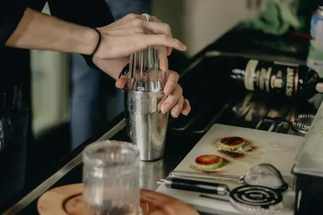 Barman przygotowuje drinka, mieszając w shakerze składniki na wódkę z colą. Na blacie leży butelka whiskey.