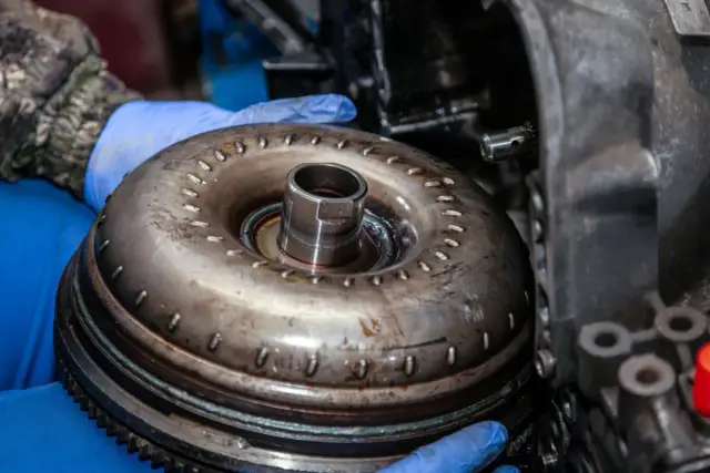 Mechanik w niebieskich rękawiczkach trzyma sprzęgło hydrokinetyczne. Gdy padnie dwumasa, może to oznaczać problemy z płynną jazdą.