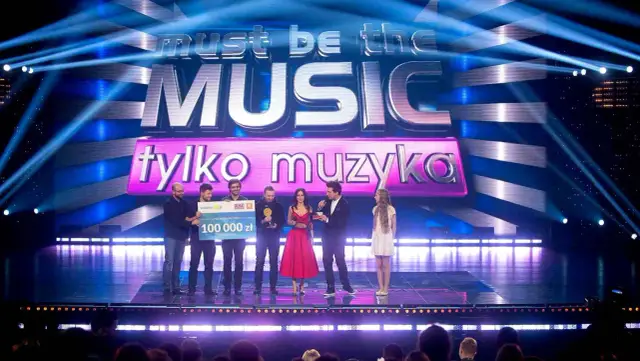 Zwycięzcy "Must be the music. Tylko muzyka" odbierają nagrodę 100 000 zł na scenie, oświetlonej niebieskimi światłami.