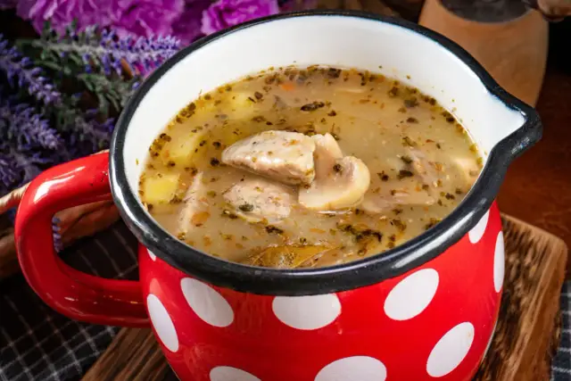 Pyszna zupa grzybowa z kawałkami mięsa i ziemniaków w czerwonym kubku w białe kropki. Zastanawiasz się, ile można trzymać zupę w lodówce?
