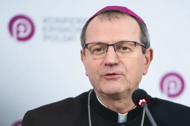 Biskup w okularach i fioletowej zuce, najmłodszy biskup w Polsce, przemawia do mikrofonu.