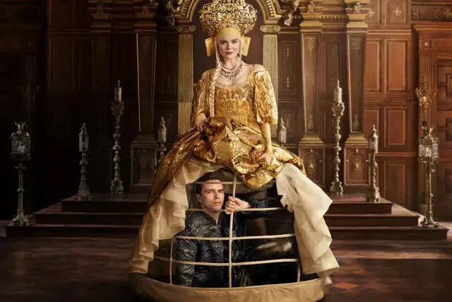 Elle Fanning w złotej sukni, z mężczyzną w klatce pod spodem. Scena z jej filmów, seriali i programów.
