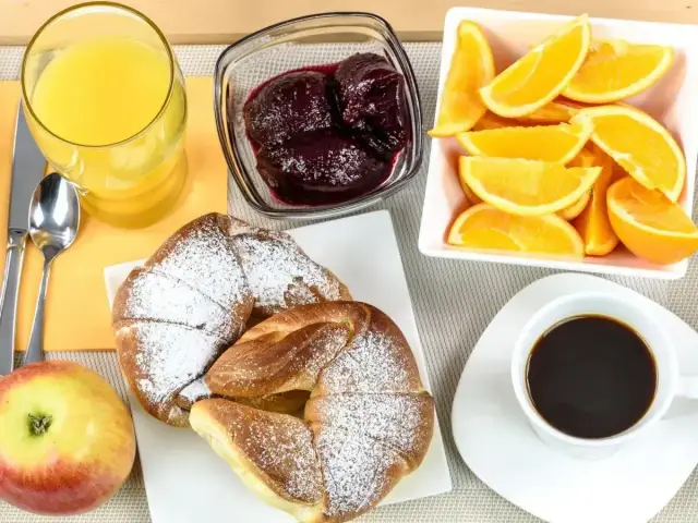 Pyszne śniadanie kontynentalne: rogaliki z cukrem pudrem, dżem, pomarańcze, sok i kawa.