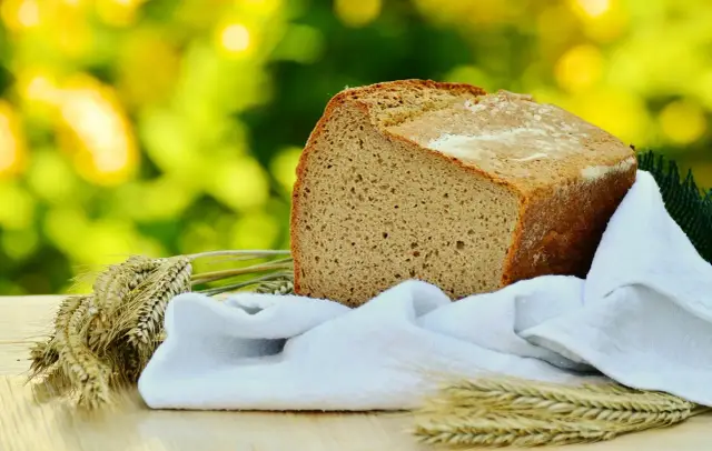 Chleb żytni, nasz codzienny chleb, na tle zieleni. Obok kłosy zbóż i biała ściereczka.
