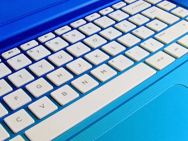 Klawiatura laptopa w kolorze niebieskim. Widoczne klawisze numeryczne i literowe. Dowiedz się, jak rozjaśnić ekran w laptopie, szukając odpowiednich skrótów klawiszowych.