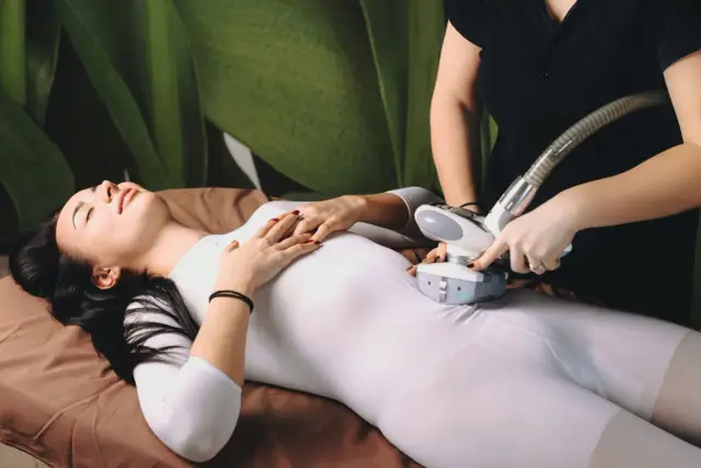 Kobieta w białym kombinezonie poddaje się zabiegowi endermologii. Terapeuta wykonuje masaż urządzeniem. Warto znać endermologia przeciwwskazania.