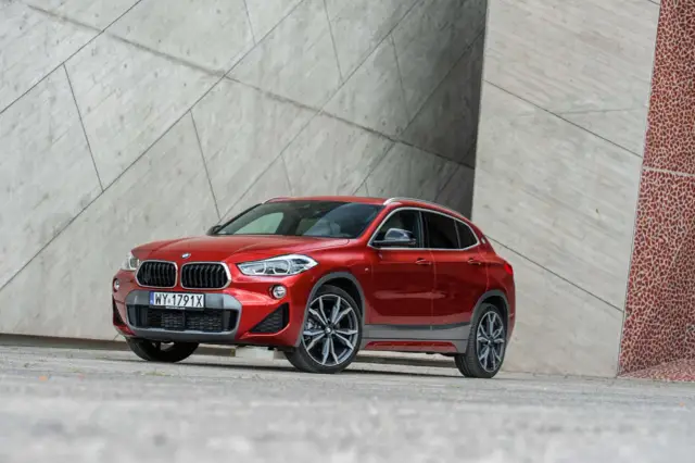Czerwone BMW X2 2025 z nowoczesnym designem, zaparkowane przy betonowej ścianie.