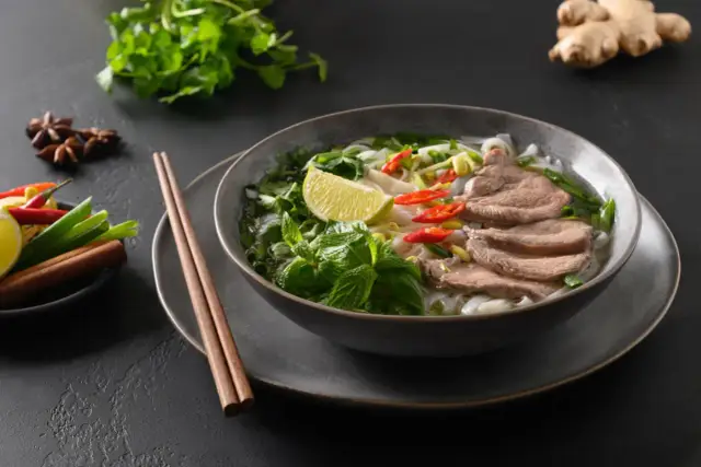 Aromatyczne pho z wołowiną, makaronem ryżowym, świeżą miętą, kolendrą, chili i limonką. Obok pałeczki i przyprawy.