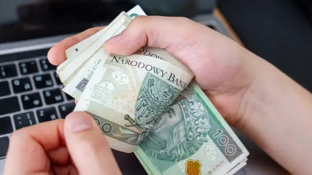 Dłonie trzymają plik banknotów 100 zł. Może to być zapłata za usługi, np. opłata reprograficzna.