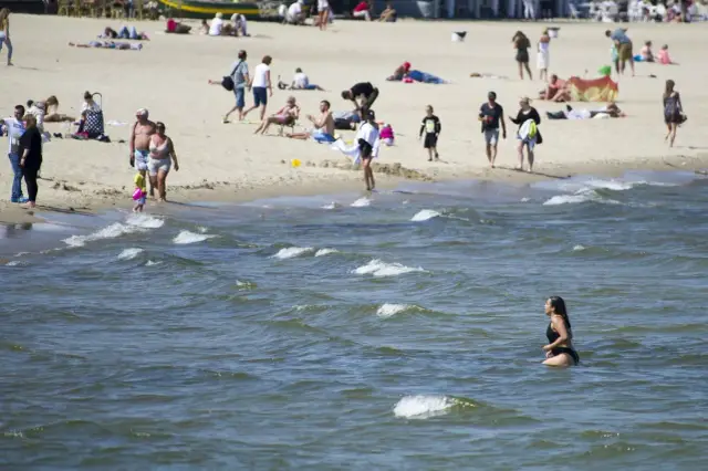 Ludzie cieszą się plażą, a jedna kobieta kąpie się w Bałtyku. Idealna temperatura wody w Bałtyku latem zachęca do relaksu.