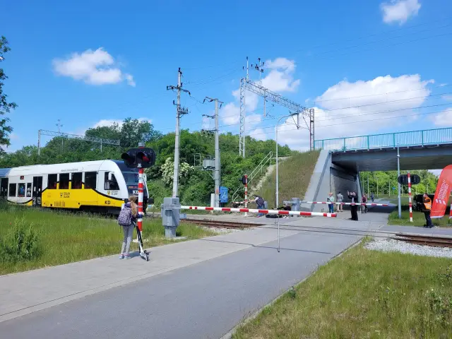 Dziewczynka na hulajnodze czeka przy przejeździe kolejowym PKP, gdy nadjeżdża pociąg.