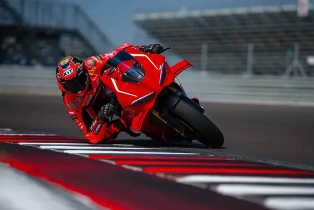 Motocyklista w czerwonym kombinezonie pochyla się na torze wyścigowym na swoim Ducati Panigale V4.
