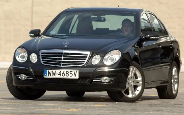 Czarny Mercedes w211 z kierowcą za kierownicą, zaparkowany na zewnątrz.