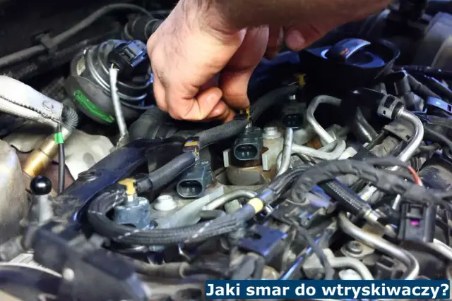 Dłoń mechanika pracuje przy silniku, podłączając wtryskiwacze. Kluczowe jest użycie odpowiedniego smaru do wtryskiwaczy, by zapewnić ich prawidłowe działanie.