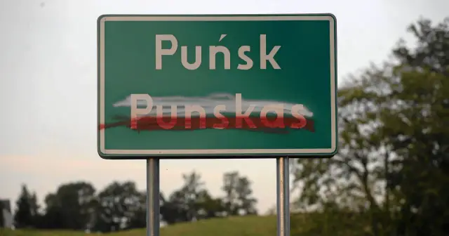Znak drogowy z napisem "Puńsk" i "Punskas", częściowo zamalowany czerwoną farbą, symbolizuje napięcia związane z mniejszością narodową.