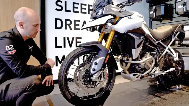 Mężczyzna w czarnej kurtce ogląda biały motocykl Triumph Tiger 900.