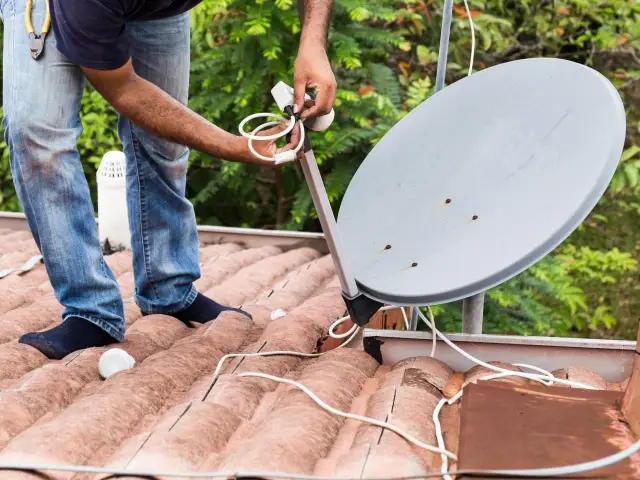 Instalator reguluje uchwyt anteny satelitarnej na dachu.