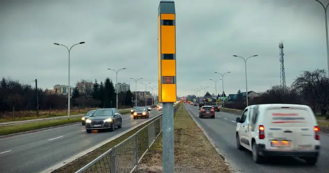 Żółty słup z urządzeniem multaradar cd. monitoruje ruch na drodze. Samochody jadą w obu kierunkach.