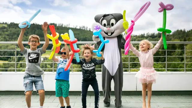 Dzieci z animatorami w strojach postaci z balonami w rękach, radośnie świętują, jakby to był ostatni dzień wakacji.