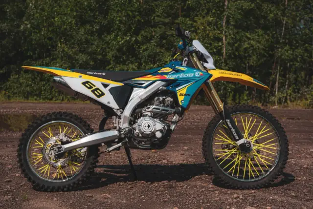 Motocykl crossowy Barton MZK 250 w kolorach niebieskim, żółtym i białym, z żółtymi szprychami.