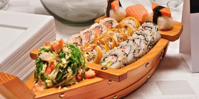 Drewniana łódka pełna sushi, przypominająca o tradycji, skąd pochodzi sushi. Różnorodne rolki i nigiri kuszą smakiem.