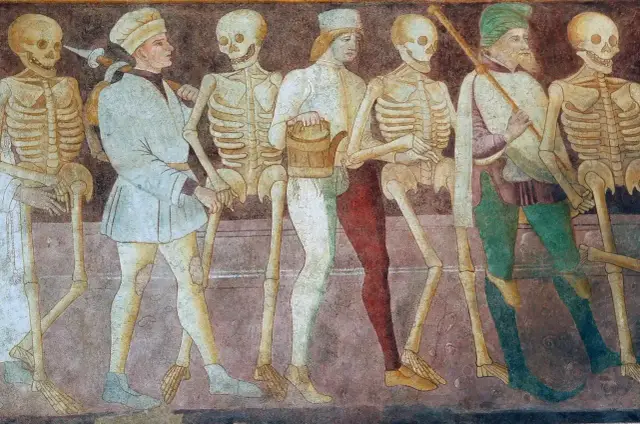 Szkielety i ludzie w średniowiecznych strojach idą w pochodzie. To mroczny obraz danse macabre, przypominający o nieuchronności śmierci.