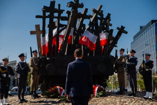 Uroczystość 1 września przy Pomniku Powstania Warszawskiego. Warty honorowe i mężczyzna w garniturze oddają hołd.