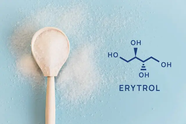 Drewniana łyżka z kryształkami i wzór chemiczny erytrytolu. Co to jest erytrytol? To słodzik.