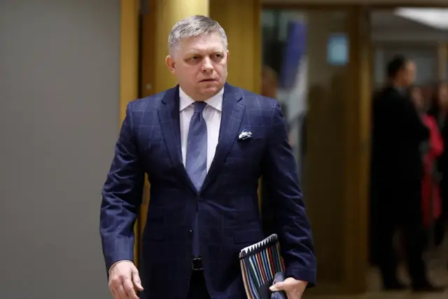 Robert Fico, prezydent Słowacji, w eleganckim garniturze idzie korytarzem, trzymając teczkę z dokumentami.