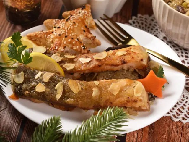 Pyszny karp z grilla, podany z cytryną, migdałami i świątecznym ciastkiem w kształcie choinki.