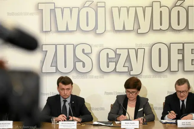 Trzech polityków siedzi przy stole. Na ścianie za nimi widnieje napis "Twój wybór ZUS czy OFE".