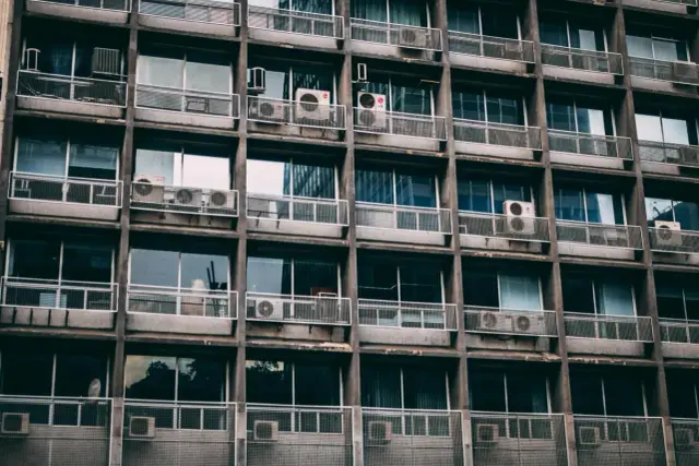 Szare okna i balkony z klimatyzatorami na betonowej fasadzie. Czy balkon wlicza się do metrażu?