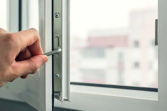 Dłoń dokręca śrubę w mechanizmie okna, przygotowując je do wymiany szyb w oknie plastikowym.