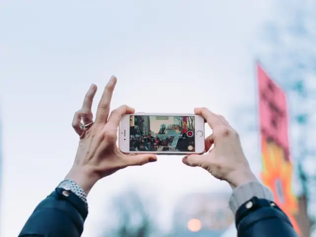 Dłonie trzymają iPhone'a w poziomie, nagrywając tłum. Dowiedz się, jak obrócić ekran w iPhone, by uchwycić szerszy kadr.