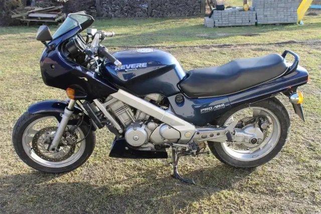 Granatowy motocykl Honda NTV Revere z napędem wałowym, zaparkowany na trawie.