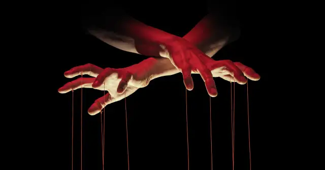 Dłonie z czerwonymi nićmi, jak marionetka, symbolizujące makiawelizm i manipulację.
