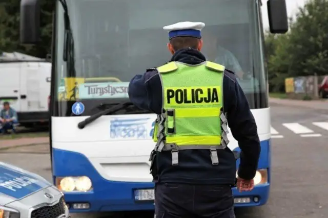 Policjant w kamizelce odblaskowej kieruje ruchem przy autokarze turystycznym. Ciekawe, ile zarabiają ochroniarze w porównaniu do jego pensji.